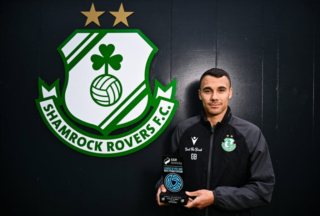 A man holding a soccer ball in front of a green and white logo.
