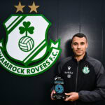 A man holding a soccer ball in front of a green and white logo.